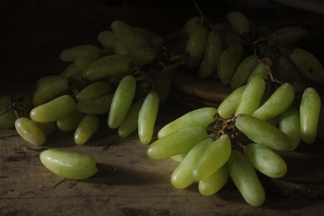 Close-up of vibrant green grapes on a rustic table in low light.